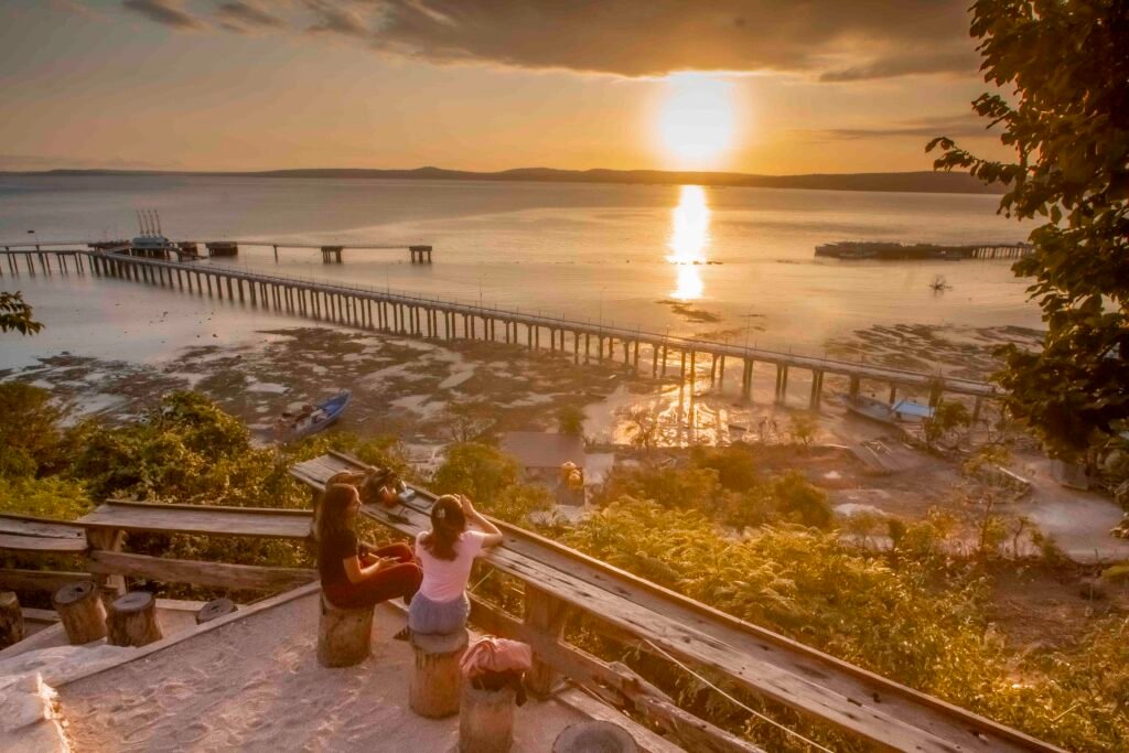 Meja dan kursi Kafe Tebing menghadap matahari rendah di atas laut