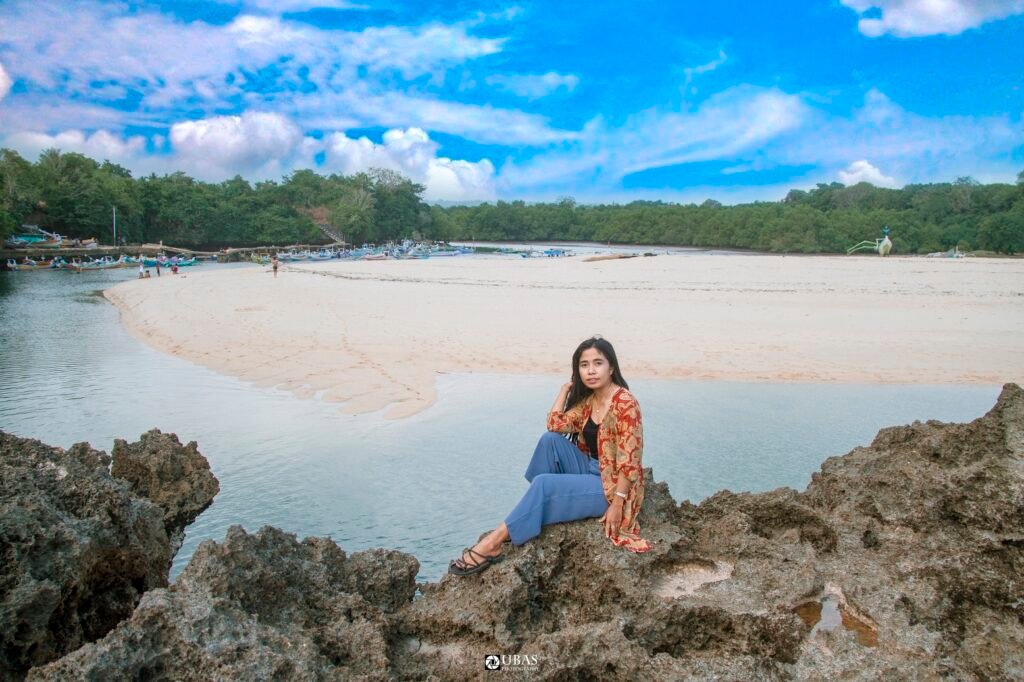 Pengunjung duduk di atas batu di tepi Pantai Pero