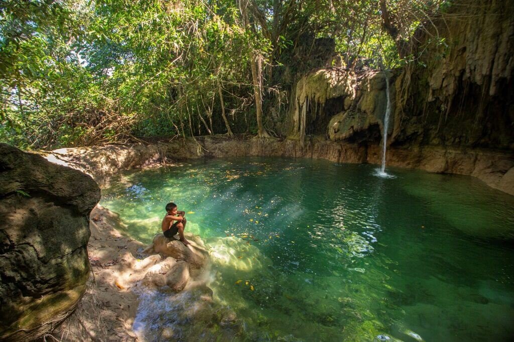 Air kolam berwarna hijau kebiruan di antara tebing dan pepohonan Pandjilu Watu